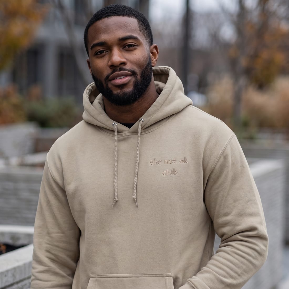 a man wearing the not ok club sandstone patch hoodie with the embroidered chest patch